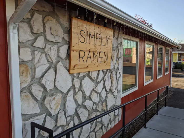 Simply Ramen's carved pine sign on the white stone wall of the barn-red building on SE Geary St